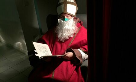 Der Nikolaus sitzt auf einem Sessel. Er hält ein aufgeschlagenes Buch in der Hand. Es ist dunkel und nur der Nikolaus ist beleuchtet.