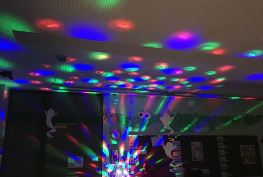 Ein dunkles Klassenzimmer wird von vielen bunten Lichtflecken einer Diskokugel erleuchtet.
