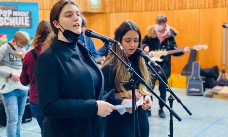 Im Vordergrund singen zwei Schülerinnen