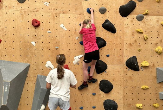 Zwei Mädchen klettern eine Boulderwand hoch.