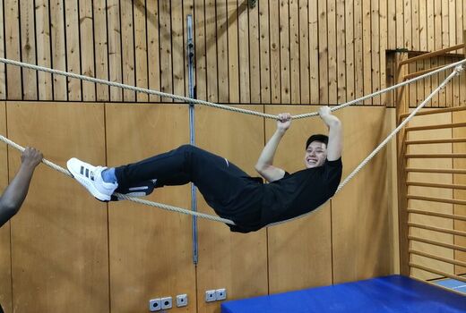 Ein Jugendlicher hängt zwischen zwei Seilen. Er lacht.