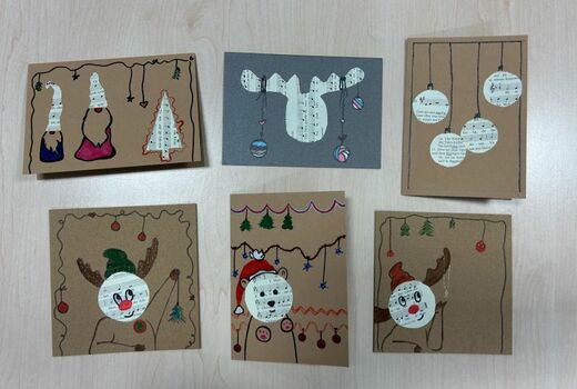 Fünf Weihnachtskarten aus braunem und eine aus grauem Karton, dekoriert mit Wichteln, Elchen, Weihnachtskugeln. Die Motive sind teilweise aus Notenpapier augeschnitten.