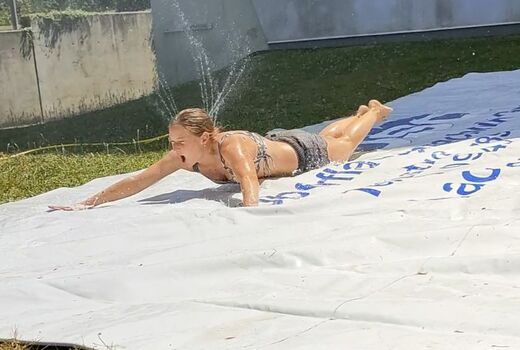 Eine Frau rutscht eine nasse Plane auf dem Bauch herunter.