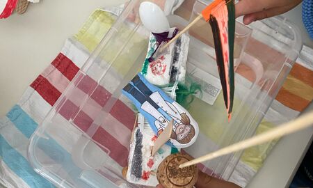 In einer durchsichtigen Kiste mit etwas Wasser schwimmt ein selbstgebautes Wasserfahrzeug. Unter der Kiste liegt ein buntes Handtuch.