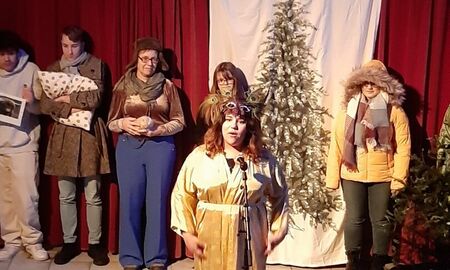 Auf dem Foto sind vekleidete SchülerInnen und ErzieherInnen beim Auftritt zu sehen. Sie stehen auf der Bühne. Im Hintergrund ist ein roter Vorhang zu sehen und ein aufgemalter Weihnachtsbaum.