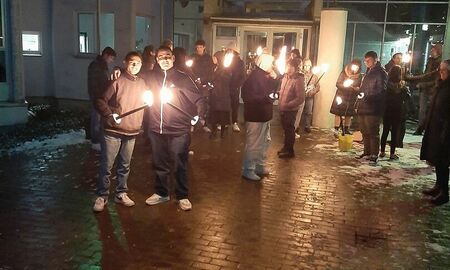 SchülerInnen stehen mit Fackeln vor dem Internatsgebäude. Die Fackeln sind angezündet und es ist dunkel.