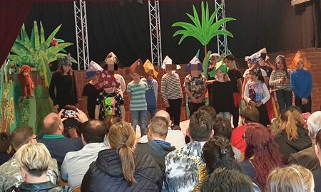 Die Schülerinnen und Schüler der dritten Klassen führen auf einer Bühne mit Palmen als Bühnenbild den neuen Erstklässlern, Erstklässlerinnen und deren Eltern mit gebastelten Piratenhüten ein Willkommensstück vor.