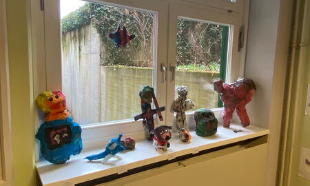 Auf einer Fensterbank stehen verschiedene bunte Kunstwerke aus Pappmaché. Ein Kunstwerk hängt am Fenster.