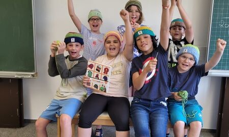 Sieben Schüler sitzen auf einem Tisch und strecken jubelnd die Hände zur Decke