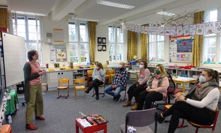 Eine Mitarbeiterin spricht vor einer fünfköpfigen Gruppe, die auf Kinderstühlen sitzt