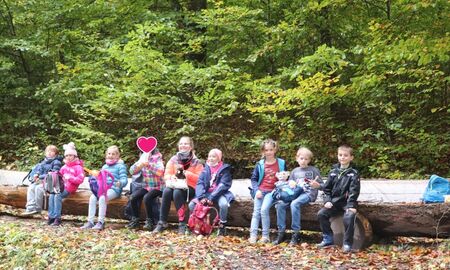 Neun Kinder sitzen in der Reihe auf dem Baumstamm