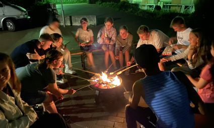 Jugendliche sitzen am Lagerfeuer und halten Stockbrot in die Glut