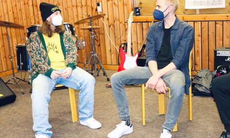 Zwei Mitglieder der Popakademie sitzen auf Stühlen und unterhalten sich