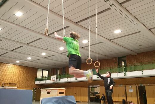 Zwei Sportler greifen im Sprung nach den Ringen.