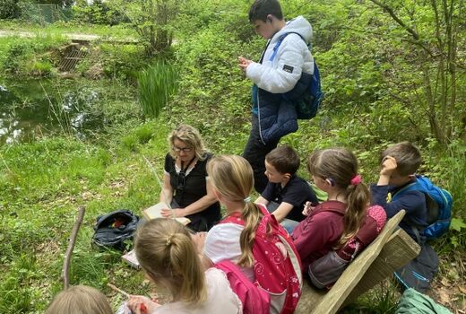 Eine Lehrerin liest einer Gruppe Kinder im Wald aus einem Buch vor