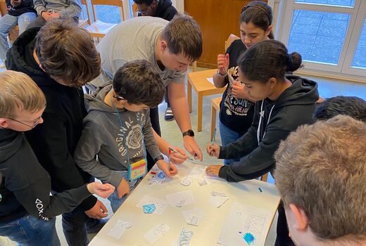 Vorstellung der SMV-Logos Schüler und Schülerinnen stehen um einen Tisch herum