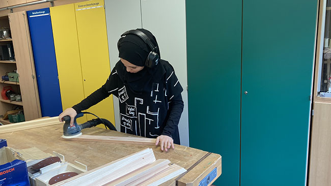 Eine Schülerin schleift das Holz ab.